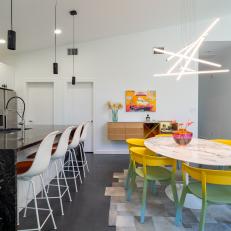 Open Plan Dining Room Features a Marble Table, Colorful Dining Chairs and a Modern Light Fixture