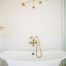 Bright Bathroom Features a Freestanding Tub With a Gold Wall-Mounted Faucet and a Gold Chandelier