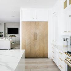 Bright Kitchen Features a White Cabinets With Gold Hardware and a Built-In Fridge 