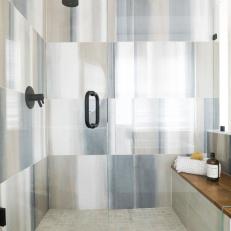 Glass Walk-In Shower Features Multicolored Tile, Black Fixtures and a Built-In Bench