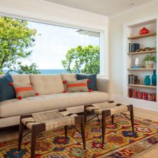 Bright Sitting Area Features a Picture Window With Waterfront Views and a Built-In Bookcase and Neutral Sofa