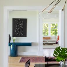 View From a Dining Room Features a Bright Hallway With Modern Art and a Lacquered Console Table