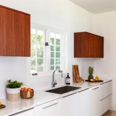 Bright Kitchen Features Wood Upper Cabinets and Modern White Lower Cabinets With a Built-In Sink and Chrome Faucet
