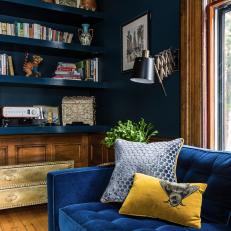 Blue Velvet Sofa Sits in a Midcentury Modern Living Room That Features Traditional Wainscoting and a Built-In Bookshelf