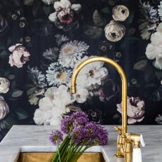 Brass Undermount Sink With Matching Fixtures Sits Below a Marble Countertop Next to a Floral Accent Wall
