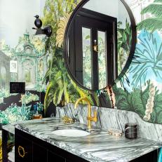 Bathroom Features Eclectic Wallpaper, an Antique Vanity With Marble Countertops and a Round Black Mirror