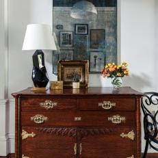 An Antique Chest Sits Against a White Wall With a Modern Piece of Art and Decorative Accents Sitting on Top
