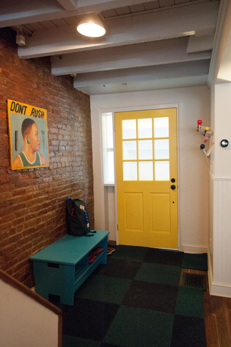 This mudroom entrance features a yellow door and exposed brick.