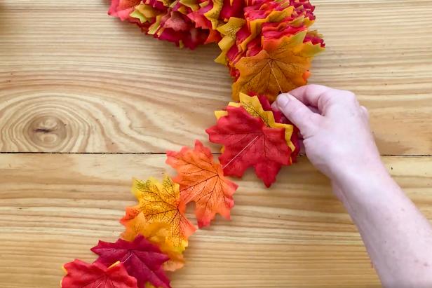 Gather together the faux fall leaves and separate by matching color. Create a stack of 12 each in your preferred color pattern so the process moves quickly. Then, use a needle and thread to pierce through the stack of grouped leaves.