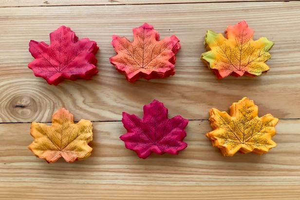 Gather together the faux fall leaves and separate by matching color. Create a stack of 12 each in your preferred color pattern so the process moves quickly. Then, use a needle and thread to pierce through the stack of grouped leaves.