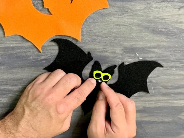 With a pair of wire cutters, cut off the backside of the miniature sunglass button so they will lie flat. Glue the glasses on the center of the face of the black felt bat with a hot glue gun. Hot glue the nose directly underneath the glasses. TIP: No mini sunglasses? Use two beads instead. No animal nose? Use a button or cut an upside-down triangle out of felt.