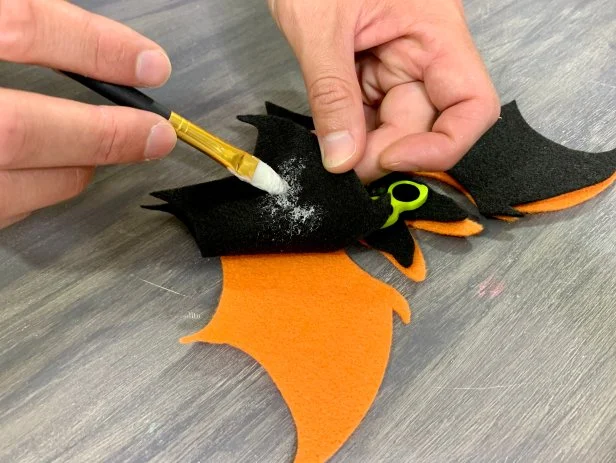 Use a paintbrush to add a light coating of felt glue to the back of the black felt bat. Slightly overlap the black felt bat with the orange bat allowing a little pop of color to peek out.