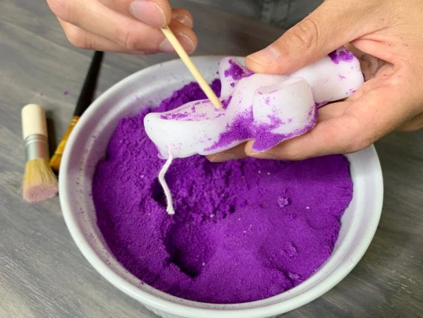 The paraffin wax will slightly shrink when cooling and separate from the sand. Once hardened, carefully remove the candle from the mold. Use a paintbrush with stiff bristles to brush off leftover stubborn sand that is stuck to the candle. Use the wooden skewer to help remove sand from any detailed areas. Carefully break away any wax that over spilled in the mold. TIP: If your candle doesn’t stand, use a sharp knife to carefully cut a straight edge for the base.