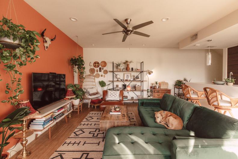 Boho living room features orange accent wall and forest green sofa