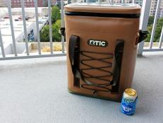 Brown RTIC cooler backpack on patio and drink in a Shark Week koozie