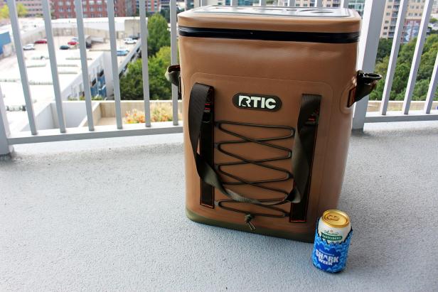 Brown RTIC cooler backpack on patio and drink in a Shark Week koozie