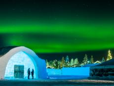 Bright green bands of light above a blue-lit ice structure and trees.