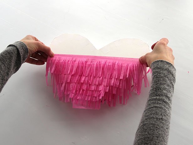 Starting at the bottom of the heart, use a glue tape roller to attach the fringe to the heart. Continue adding the fringe, layering as you go. Repeat this process on the other side. Finally, trim the edges for a neater look.