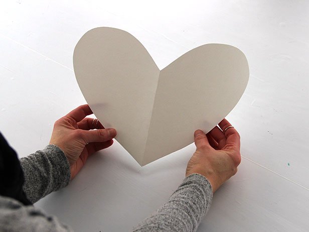 Fold a piece of card stock in half, and use scissors to cut a half-heart shape along the folded edge of the paper. Unfold the paper and trim if needed.