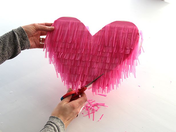 Starting at the bottom of the heart, use a glue tape roller to attach the fringe to the heart. Continue adding the fringe, layering as you go. Repeat this process on the other side. Finally, trim the edges for a neater look.