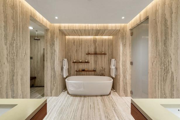 Dramatic, striped warm stone surrounds  tub and floating shelves.