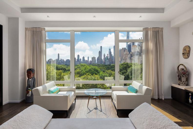 A symmetrical white living room with large windows overlooking a park.