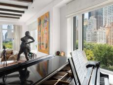 Metal sculptures sit atop a black piano in a large white living room.