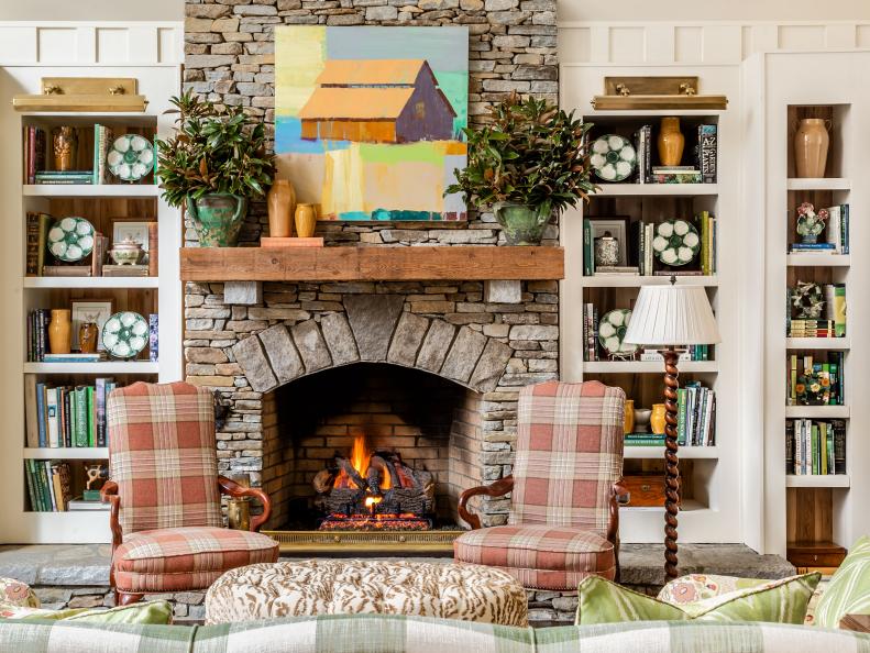 Red buffalo plaid armchairs in front of stone fireplace and painting. 