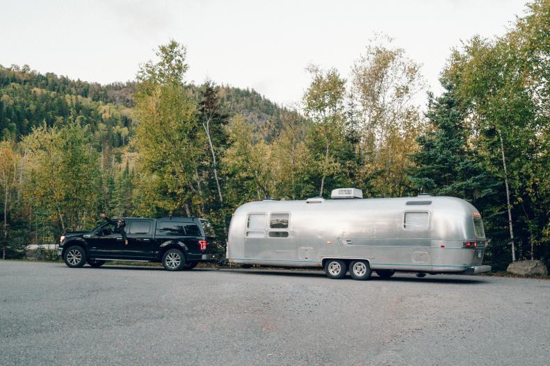 A truck pulling an Airstream Trailer parked near a forest.