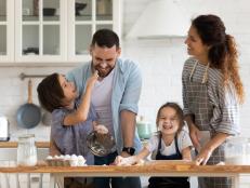 A family with two young children bakes together in a kitchen.