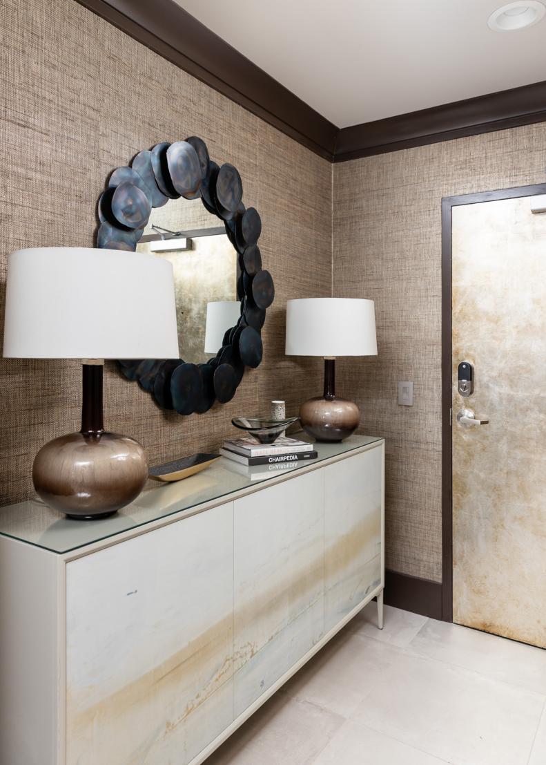 Room with textured beige wallpaper, dark molding, mirror & gold door.