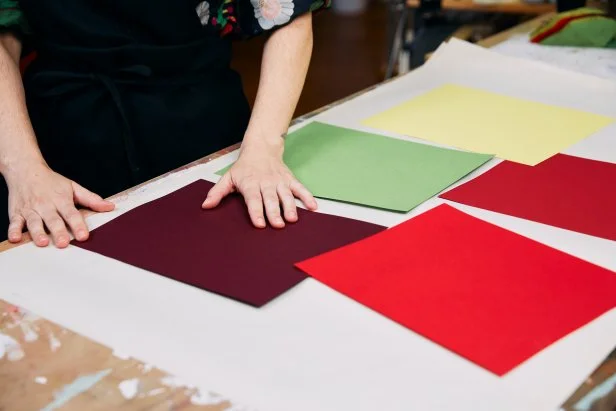 Woman Places Red, Yellow, Green and Burgundy Papers on Table
