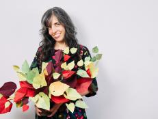 Woman Holds Red, Green and Yellow Paper Plant While Smiling for Camera