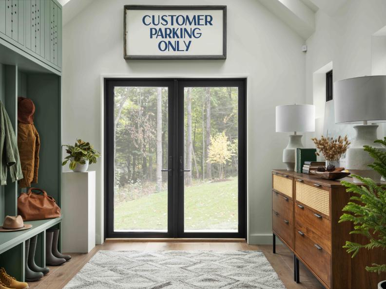 Sleek glass and metal double doors open up to the entry of this modern-meets-classic luxury cabin, an organized and stylish space with airy white walls, built-in mossy green mudroom, and A-frame ceiling.