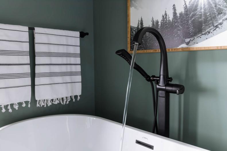 An elegant matte black tub filler with clean, modern lines behind the tub includes a smooth single lever handle design, and hand shower for full body spray. 
