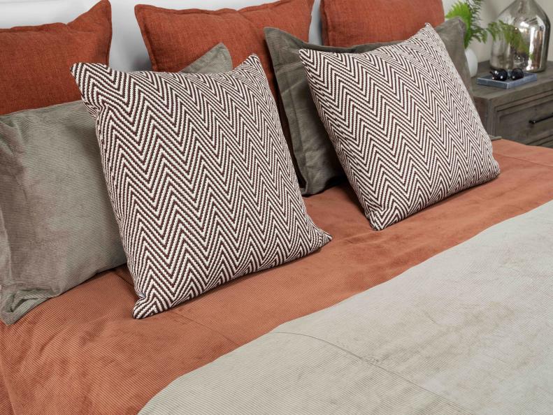 Throw pillows with an on-trend chevron pattern and moss green hue fit the autumnal color scheme of the bed, and provide contrast for the warm tones of the terra cotta duvet cover set.