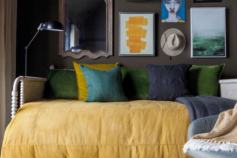 A bold, yellow comforter on the daybed adds warmth and plays off the sunny tones found in the artwork hung in the upstairs guest bedroom. Jewel toned pillows add a soft accent and enhance the den-like feel the space evokes.