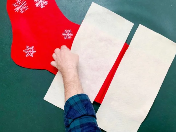 Create a folded white brimmed detail for the top of the stocking. Cut out two panels of white felt that are the same width of the top of the stocking and about six inches deep. Fold down the top of the stocking, apply a thin coating of fabric glue with a paint brush and press down the white felt lining the edges. Repeat this process with the back panel.