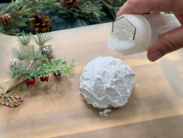 Add a snowy look to round half floral foam with textured snow paint. Use a lot of paint and apply it to the foam with a craft stick for a truly organic look. Once done, add a sprinkle of glitter for some extra sparkle. Tip: If you have trouble finding textured snow paint add baking soda to acrylic paint for some texture.