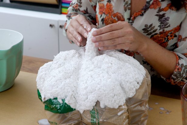 Working in small sections, form the paper mache onto the pumpkin. Cover the top half of the pumpkin, saving the stem until last so you can use it to turn the pumpkin around. Be sure to mold the paper mache into the ridges to keep the pumpkin shape. Set aside to let dry completely, which could take a full day or two.