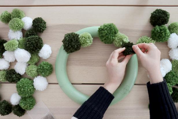 Use U-shaped pins and normal sewing pins to pin the pom poms onto the wreath form. Make sure they’re placed closely next to each other so the foam doesn’t show through. Add pom poms around the sides of the wreath to get an even and full look.