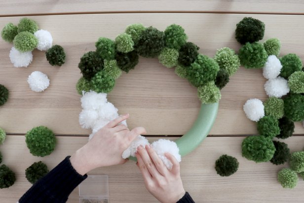 Use U-shaped pins and normal sewing pins to pin the pom poms onto the wreath form. Make sure they’re placed closely next to each other so the foam doesn’t show through. Add pom poms around the sides of the wreath to get an even and full look.