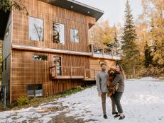 Couple Stands In Front of Custom Cabin in Alaska with Fluffy Dog