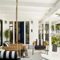 A Bright Covered Porch Features a Small Sitting Area With Wicker Chairs and a Wood Table and a Hanging Daybed 