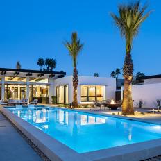 A Modern Cement Swimming Pool Is Surrounded By Stone Pavers, Landscape Lighting and Towering Palm Trees