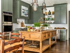 Dusty green kitchen with warm toned island and copper pendants. 