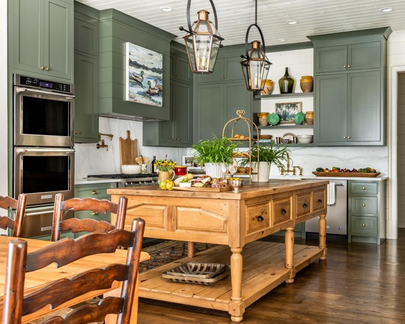 Dusty green kitchen with warm toned island and copper pendants. 