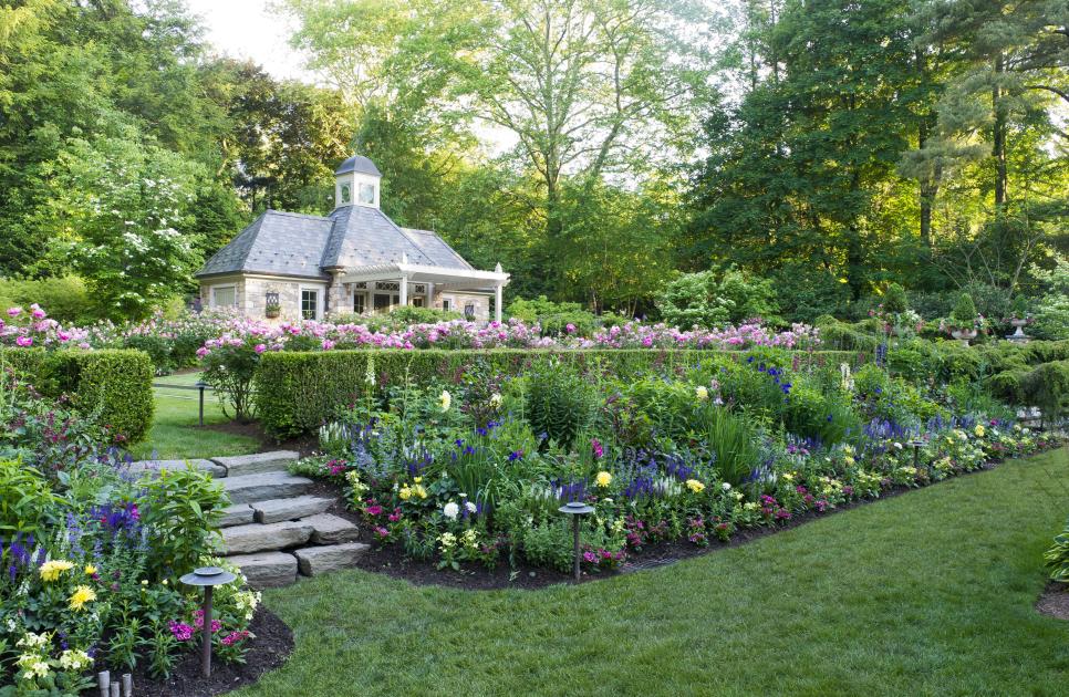 A Lush Backyard Garden Features Tiered, Flower-Filled Garden Beds and a Large Stone Garden House