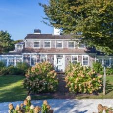 A Cape Cod-Style Home Features a Brick Walkway, a Circle Gravel Driveway and Lush Hydrangea Bushes