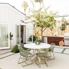 A Cottage-Style Backyard Features a Cement Patio, an Outdoor Dining Furniture and an Outdoor Kitchen